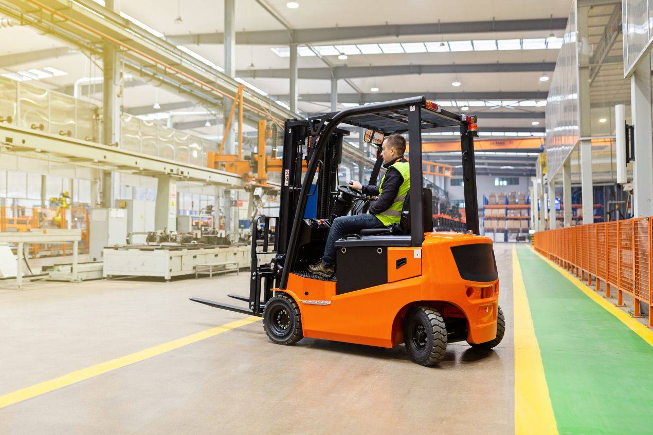 Fahrer mit Warnweste bedient gemieteten Gabelstapler in Produktionshalle