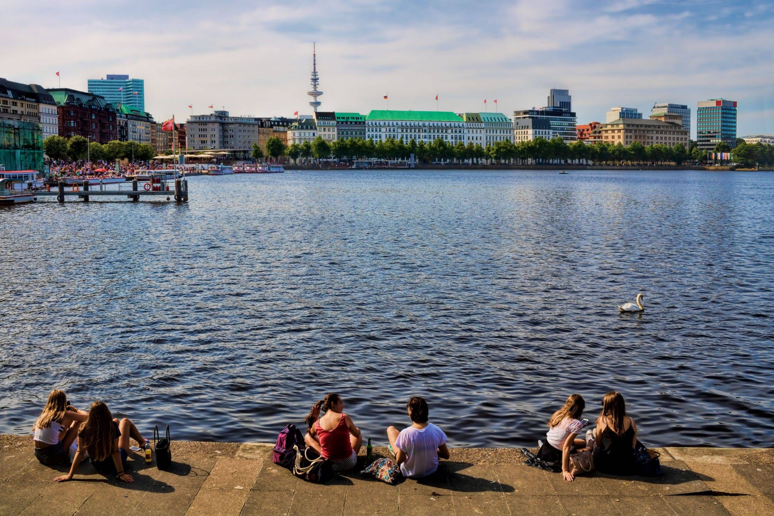 Jugendliche sitzen an der Binnenalster in Hamburg mit Blick auf die Skyline und den Fernsehturm